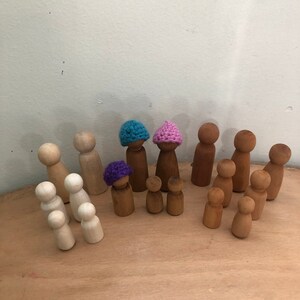 May include: A collection of wooden peg dolls, some wearing crocheted hats in purple, pink, and blue. The dolls are arranged on a wooden surface.