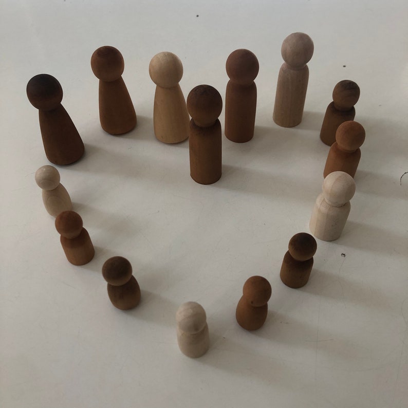 May include: A collection of wooden figurines in brown and natural wood tones arranged in a heart shape on a white surface.