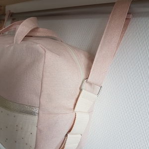 May include: A pink canvas duffel bag with a white strap and silver hardware. The bag has a zipper closure and a gold trim.