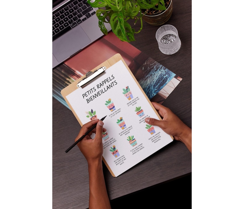 May include: A wooden clipboard with a printed sheet featuring illustrated potted plants and the text "PETITS RAPPELS BIENVEILLANTS". A person is holding the clipboard and writing with a black pen. A laptop and a potted plant are in the background.
