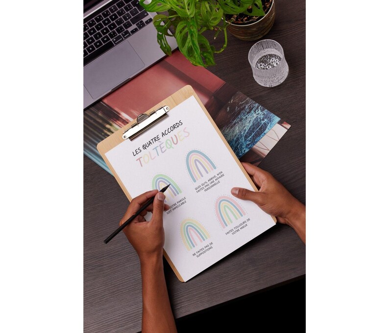 May include: A clipboard with a white sheet of paper on it. The paper has the title "Les Quatre Accords Tolteques" written in black. There are four rainbow illustrations on the paper, each with a different colored background. The text below each rainbow is in French.