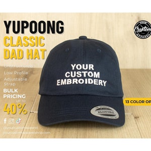May include: A navy blue unstructured dad hat with an adjustable strap. The hat has white embroidery that says "YOUR CUSTOM EMBROIDERY".