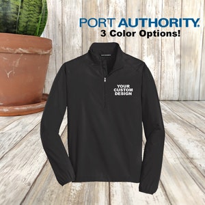 May include: Black quarter-zip pullover with long sleeves. The pullover has a zippered neck and a small white logo that says "YOUR CUSTOM DESIGN".