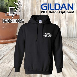 May include: Black hooded sweatshirt with a pocket on the front. The text "YOUR CUSTOM DESIGN" is embroidered on the pocket in white.