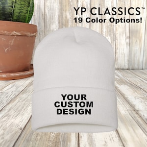 Op de afbeelding: Witte beanie met de tekst "YOUR CUSTOM DESIGN" in zwarte letters.