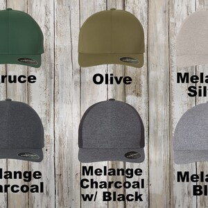 May include: Six baseball caps in different colours. The caps are all the same style, with a curved brim and a mesh back. The colours are spruce, olive, melange silver, melange charcoal, melange charcoal with black mesh, and melange blue.
