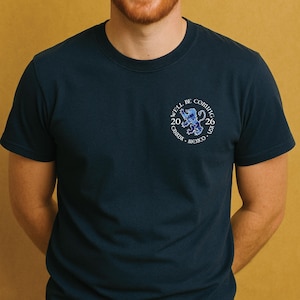 May include: Navy blue t-shirt with a small graphic on the chest. The graphic includes the text "WE'LL BE COMING 2026" and a map design with the words "CANADA, MEXICO, USA."