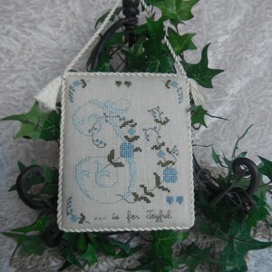 May include: A white fabric sampler with a blue and green embroidered letter J and the text "... is for Joyful".