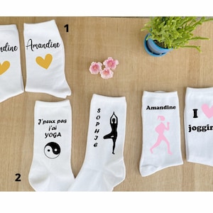 Peut inclure: Ensemble de six paires de chaussettes blanches avec différents motifs. Les chaussettes présentent un cœur jaune, un symbole yin yang noir, une silhouette noire d'une personne faisant du yoga, une silhouette rose d'une personne courant, un cœur rose et le texte "J'aime le jogging".
