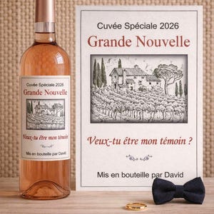 Può includere: Una bottiglia di vino rosato e un biglietto con la scritta "Grande Nouvelle" e un'illustrazione di un vigneto. Il biglietto include anche la scritta "Veux-tu être mon témoin?" e un papillon e un anello d'oro sul tavolo.