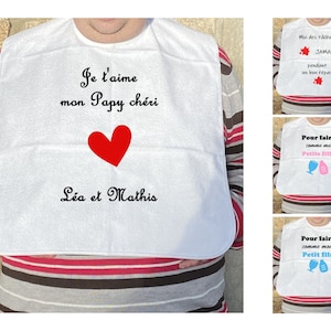 Peut inclure: Bavoir blanc avec le texte "Je l'aime mon Papy chéri" et un cœur rouge. En dessous du texte se trouve "Léa et Mathis".