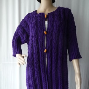 Peut inclure: Un cardigan en tricot violet avec un motif en câble et des boutons orange.