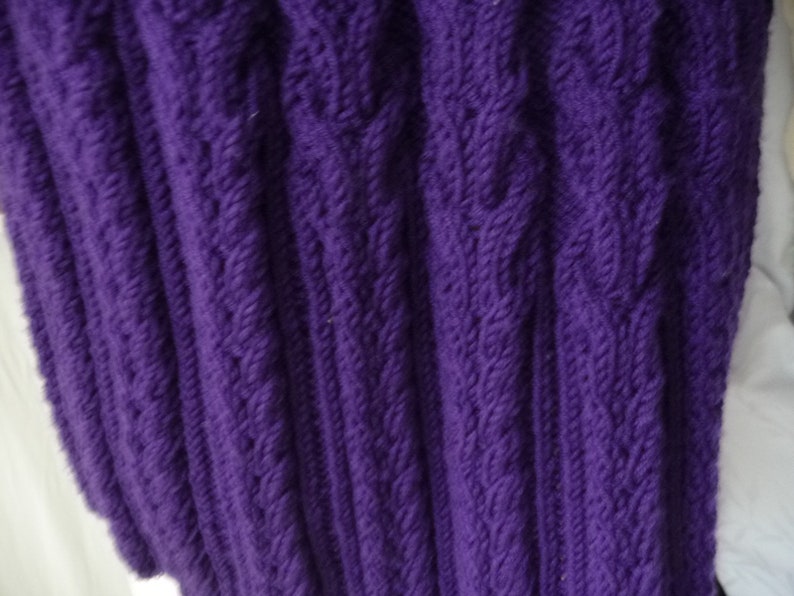 May include: Purple knitted fabric with a cable knit pattern.