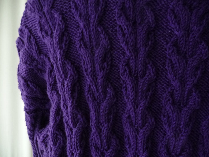 May include: Purple knitted sweater with a cable knit pattern.