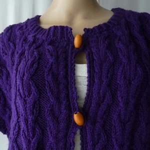 May include: Purple knitted cardigan with a cable knit pattern and wooden buttons.