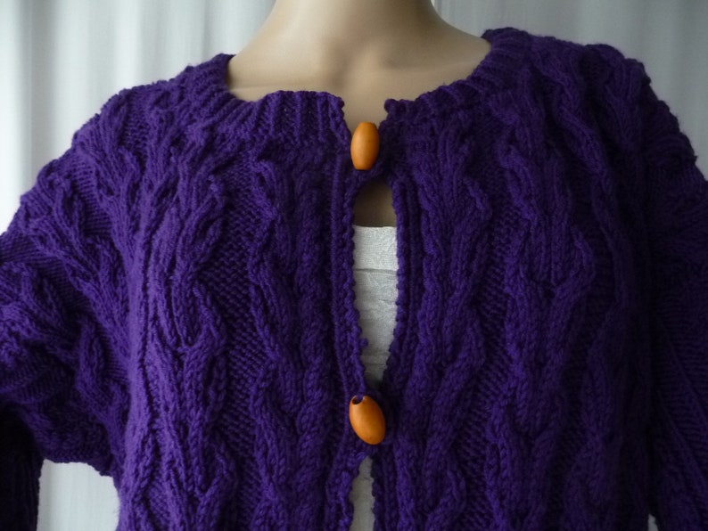 May include: Purple knitted cardigan with a cable knit pattern and wooden buttons.