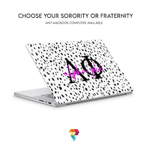 Puede incluir: Un portátil blanco con un diseño de estampado de dálmata en blanco y negro. El portátil tiene un logotipo rosa "Alpha Phi" en la parte posterior.