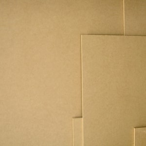 May include: A collection of beige-colored, rectangular sheets of paper or cardboard, arranged in a layered composition. The sheets vary in size and are stacked together, creating a textured surface. The image showcases the material's color and texture.