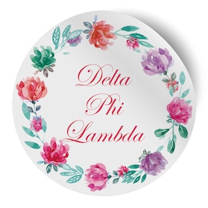 May include: A white circle with a floral wreath border in shades of pink, red, and green. The text "Delta Phi Lambda" is written in red cursive lettering inside the wreath.