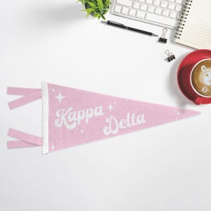 Könnte beinhalten: Ein rosa Filz-Wimpel mit weißen Glitzerbuchstaben, auf dem "Kappa Delta" steht, mit weißen Glitzersternen auf rosa Hintergrund.