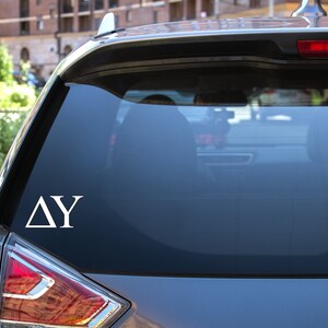 May include: A white vinyl decal with the Greek letters Delta and Gamma on a grey car.