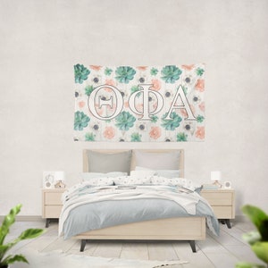 Könnte beinhalten: Eine weiße Wandbehänge mit einem floralen Muster mit grünen Sukkulenten und rosa Blüten. Die Buchstaben "ΘΦΑ" sind in Weiß vor einem Holzmaserungshintergrund.