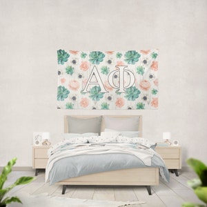 Könnte beinhalten: Eine weiße Wandbehänge mit einem floralen Muster mit Sukkulenten, rosa Blüten und weißen Blüten. Die Buchstaben "AΦ" befinden sich in der Mitte der Wandbehänge.