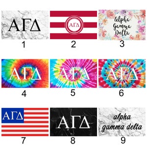 May include: Nine different designs for a sorority flag featuring the letters "ΑΓΔ" in white on various backgrounds, including marble, tie-dye, stripes, and a floral pattern. The text "Alpha Gamma Delta" is also included on one of the designs.