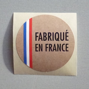 May include: A round, brown paper sticker with a red, white and blue stripe design. The sticker says "Fabriqué en France" in black text.