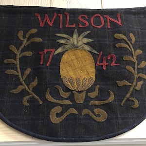Puede incluir: Un tapiz de pared de tela azul y marrón con un diseño de piña y el texto "WILSON 17 42".