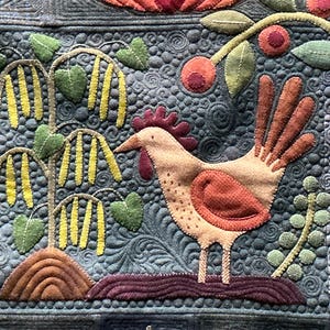 May include: A detailed textile art piece featuring a rooster, trees, and fruit. The rooster is beige with red accents, standing on a purple base. Trees with yellow and green leaves are on the left, and red fruit with green leaves are on the right.