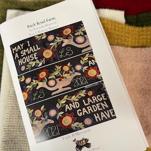 May include: A printed pattern booklet titled Back Road Farm by Lucinda Shattuck, Part 6 Bottom Banner. The cover displays three horizontal sections of dark fabric featuring embroidered flowers, vines, and the text MAY I A SMALL HOUSE AND LARGE GARDEN HAVE, LS, and 2021. The bottom includes the Triple R Mercantile logo.