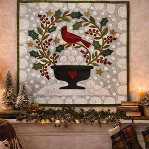 May include: A square fabric wall hanging featuring a central black pedestal bowl filled with white snowballs, topped by a red cardinal bird perched on a wreath of green holly leaves and red berries, all set against a light gray background.