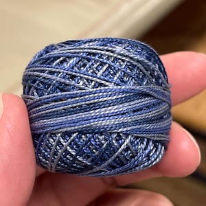 Puede incluir: Una pequeña madeja de hilo de bordar azul y gris.