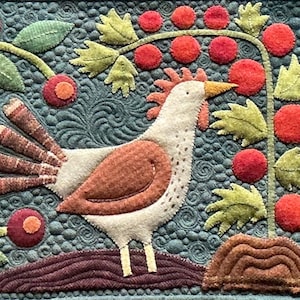 May include: A textile wall hanging featuring a cream-colored chicken with a brown wing and tail feathers, standing on a brown mound. The background is a dark teal fabric with swirling quilted patterns, decorated with red berries and green leaves.