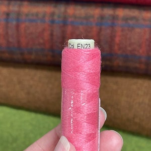 Pode incluir: Uma bobina de fio rosa com um rótulo branco que diz "Col. EN23".