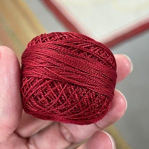 以下が含まれることがあります： 赤い刺繍糸の玉のクローズアップ。糸はきつく巻かれており、質感のある表面を示しています。色は深く、豊かな赤色で、高品質の素材を示唆しています。刺繍やその他の手芸プロジェクトに最適です。