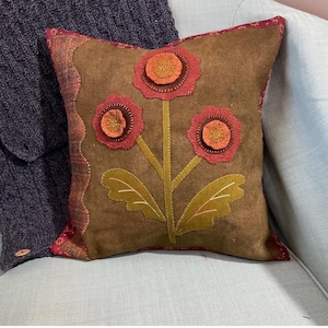 以下が含まれることがあります： 3つの赤、オレンジ、黄色の花と緑の葉が描かれた花柄の茶色のクッション。クッションは柔らかく、質感のある生地で作られています。