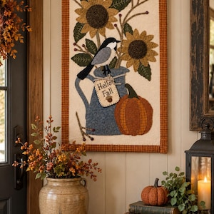 May include: A rectangular fabric wall hanging featuring a cream background with a brown checkered border. The design includes two sunflowers, a black and white bird perched on a blue pitcher, and an orange pumpkin with a tag reading Hello Fall.