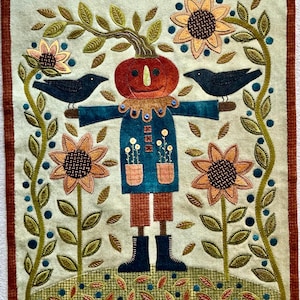Può includere: Un arazzo rettangolare in tessuto raffigurante uno spaventapasseri centrale con testa di zucca, che indossa un cappotto blu con tasche e pantaloni marroni. Due corvi neri sono appollaiati sulle braccia, circondati da girasoli e viti verdi.
