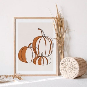 A seasonal fall print. This fall print has three pumpkins draw with a continuous black line. Random parts of the three pumpkins are painted orange and the background is a beige with a white border.