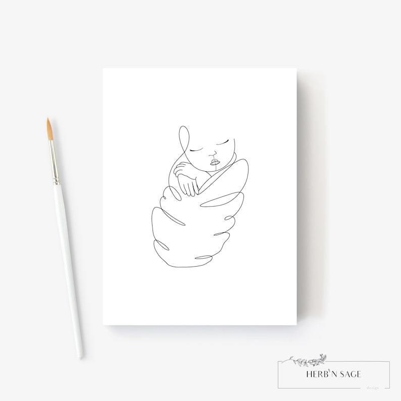 May include: A minimalist line art print of a sleeping baby swaddled in a leaf-like shape. The artwork is in black against a white background. A paintbrush is in the image. The print has the text "HERB'N SAGE design" at the bottom.