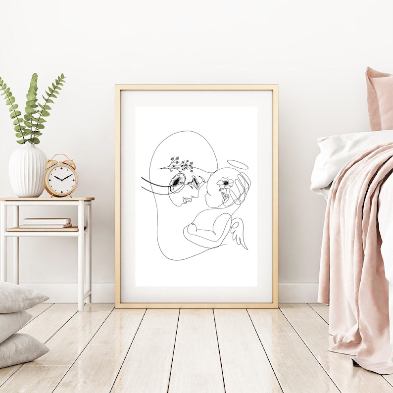 May include: A black and white line drawing of a mother holding a baby. The mother has a flower crown on her head and the baby has a halo. The drawing is on a white background.