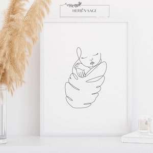 May include: A framed minimalist line art print featuring a sleeping baby. The black line drawing depicts a swaddled infant with closed eyes. The print is in a white frame, with the text "HERB'N SAGE" at the top.
