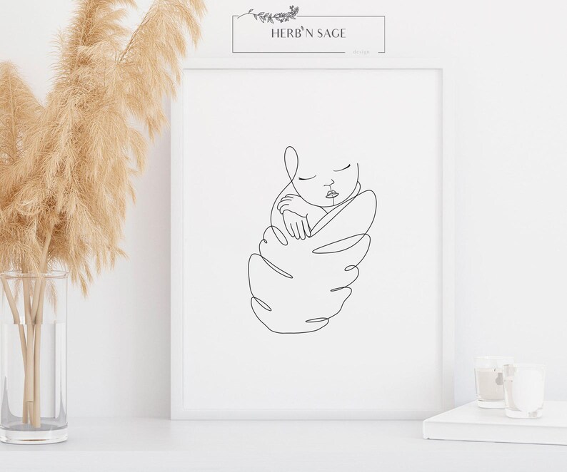 May include: A framed minimalist line art print featuring a sleeping baby. The black line drawing depicts a swaddled infant with closed eyes. The print is in a white frame, with the text "HERB'N SAGE" at the top.