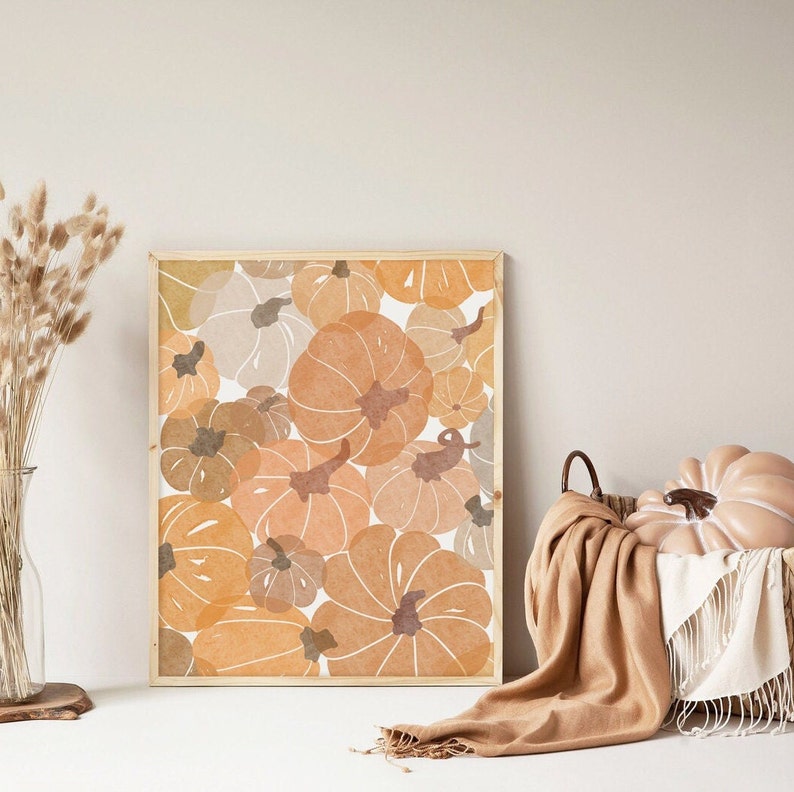 May include: A framed print featuring a pattern of orange, brown and beige pumpkins. The print is in a wooden frame and is hanging on a white wall.