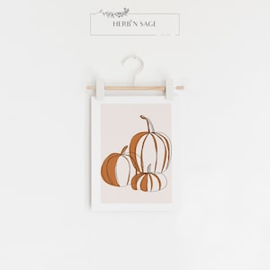 A seasonal fall print. This fall print has three pumpkins draw with a continuous black line. Random parts of the three pumpkins are painted orange and the background is a beige with a white border.