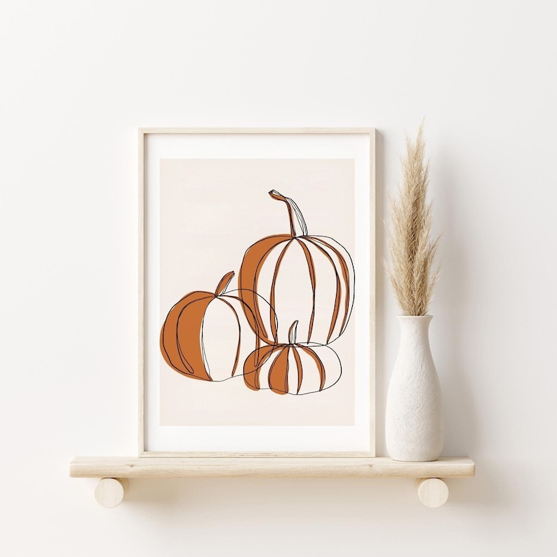 A seasonal fall print. This fall print has three pumpkins draw with a continuous black line. Random parts of the three pumpkins are painted orange and the background is a beige with a white border.