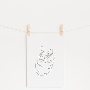 May include: A minimalist line art print of a sleeping baby, held in a swaddle. The black line drawing is displayed on white paper, held by wooden clothespins on a string. The text "HERB 'N SAGE design" is at the top.