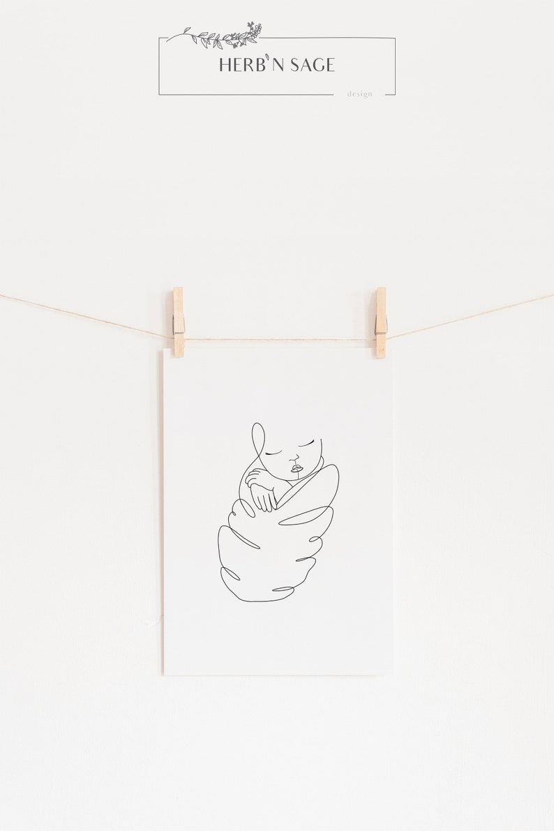 May include: A minimalist line art print of a sleeping baby, held in a swaddle. The black line drawing is displayed on white paper, held by wooden clothespins on a string. The text "HERB 'N SAGE design" is at the top.